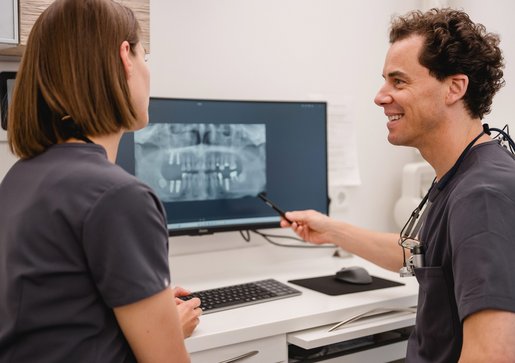Dr. Fabian Sigmund und Maja Schreiner besprechen eine digitale Röntgenaufnahme eines Kiefers auf einem Monitor.