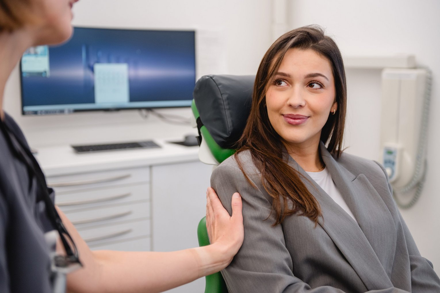 Eine Zahnärztin beruhigt eine Patientin mit Angst vorm Zahnarzt und legt eine Hand auf die Schulter.