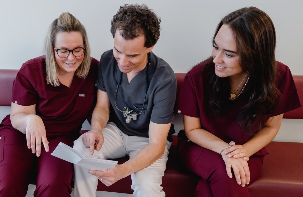 Dr. Fabian Sigmund und zwei ZFA schauen gemeinsam auf Dokumenten und besprechen diese lächelnd.