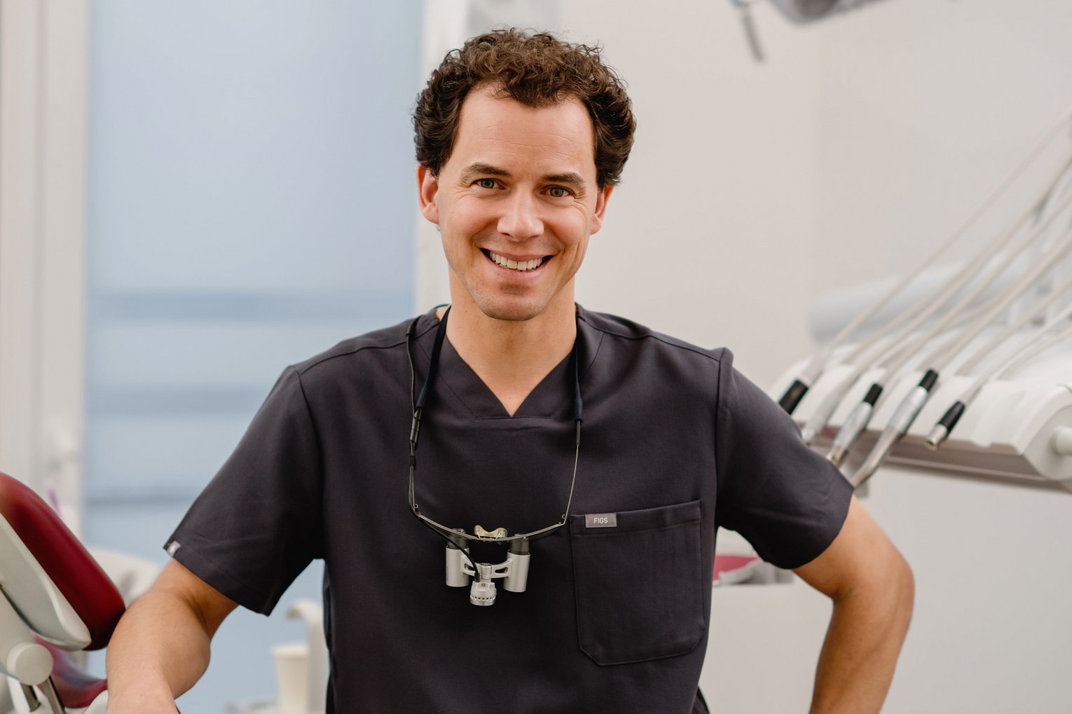 Zahnarzt Dr. Fabian Sigmund sitzt lächelnd auf einem Zahnarztstuhl in seiner Praxis.
