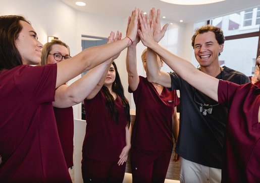 Dr. Fabian Sigmund und das Praxisteam stehen zusammen und geben sich lächelnd die Hände zum High-Five.