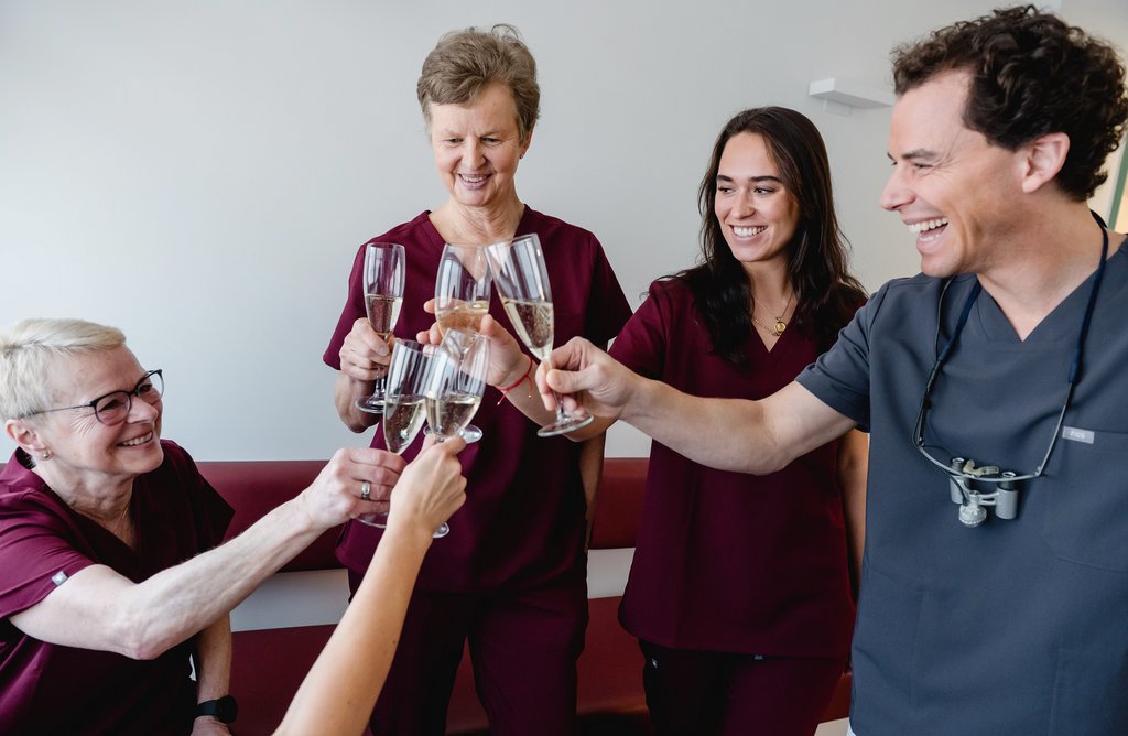 Dr. Fabian Sigmund und Team stoßen mit Sektgläsern an und lächeln, sie feiern gemeinsam einen Erfolg oder besonderen Anlass.