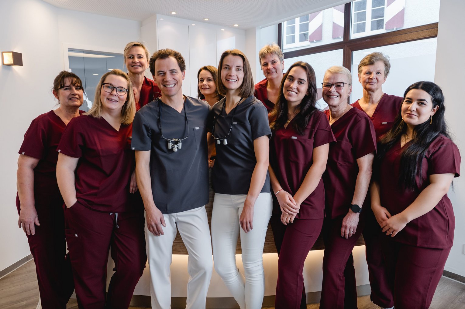 Gruppenbild des Praxisteams der Zahnarztpraxis Dr. Sigmund & Kollegen in Berufsbekleidung in einer hellen Praxis.
